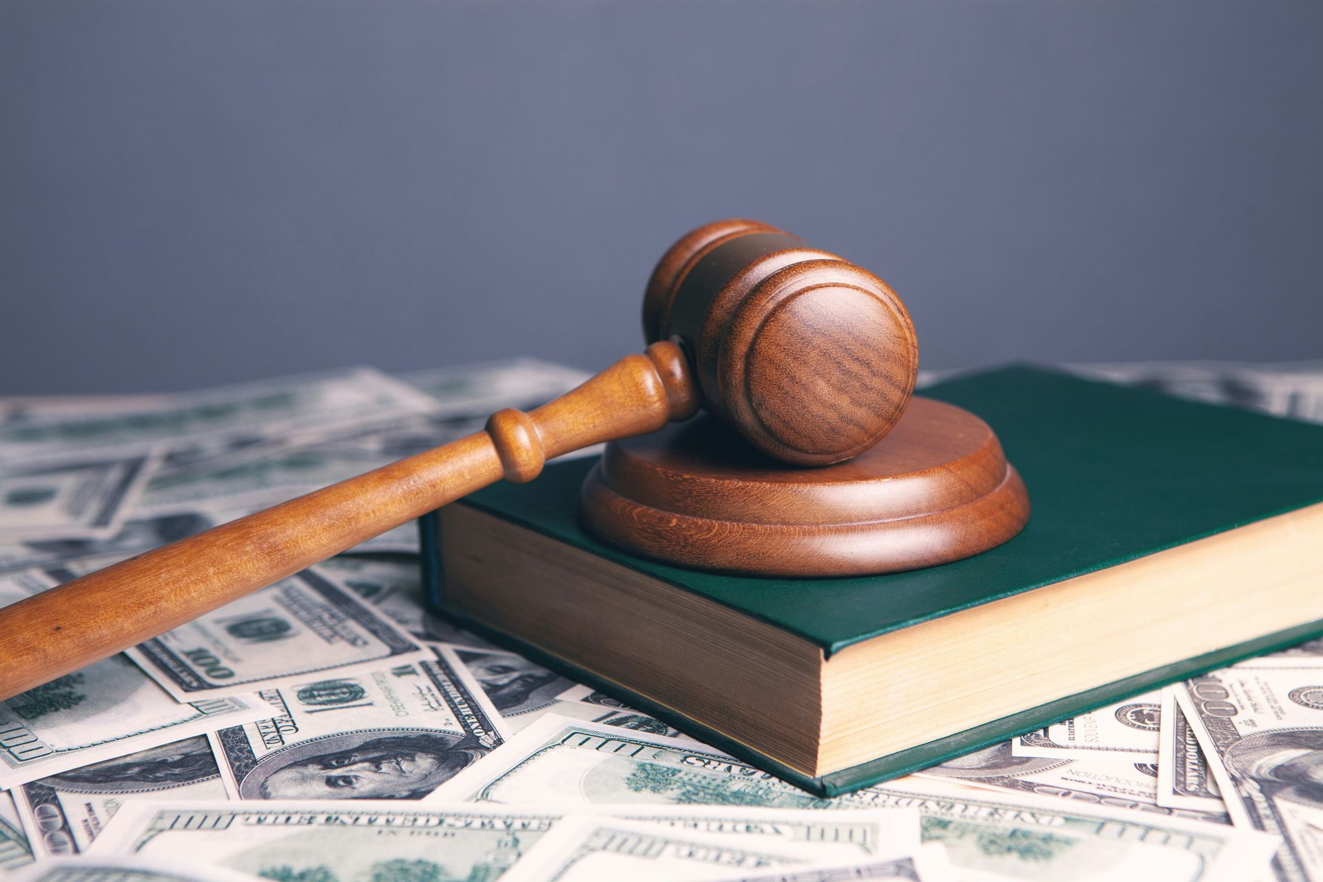 A wooden gavel resting on a green book surrounded by scattered dollar bills